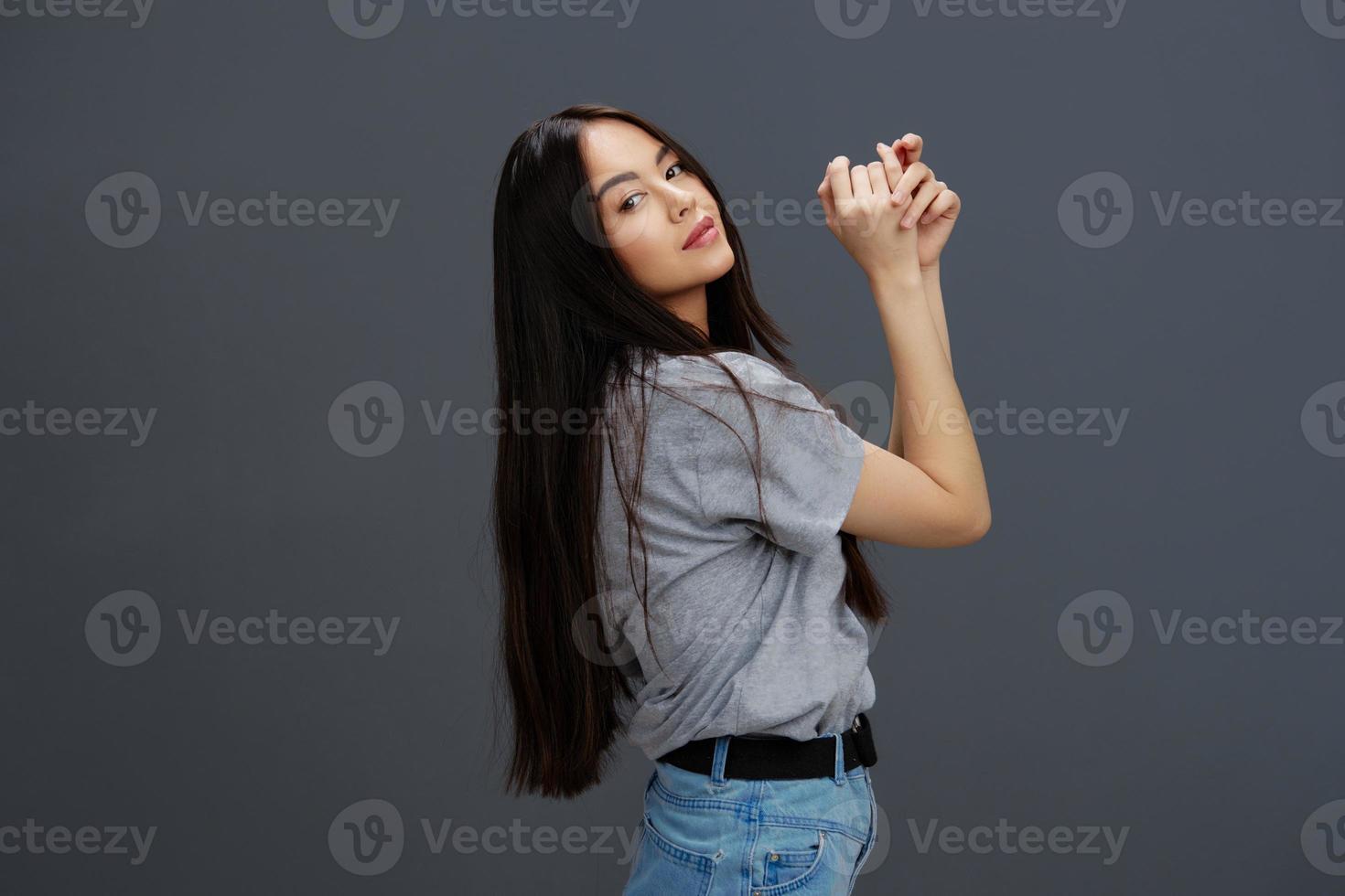 joven mujer con largo pelo en un gris camiseta gesticulando con manos gris antecedentes foto