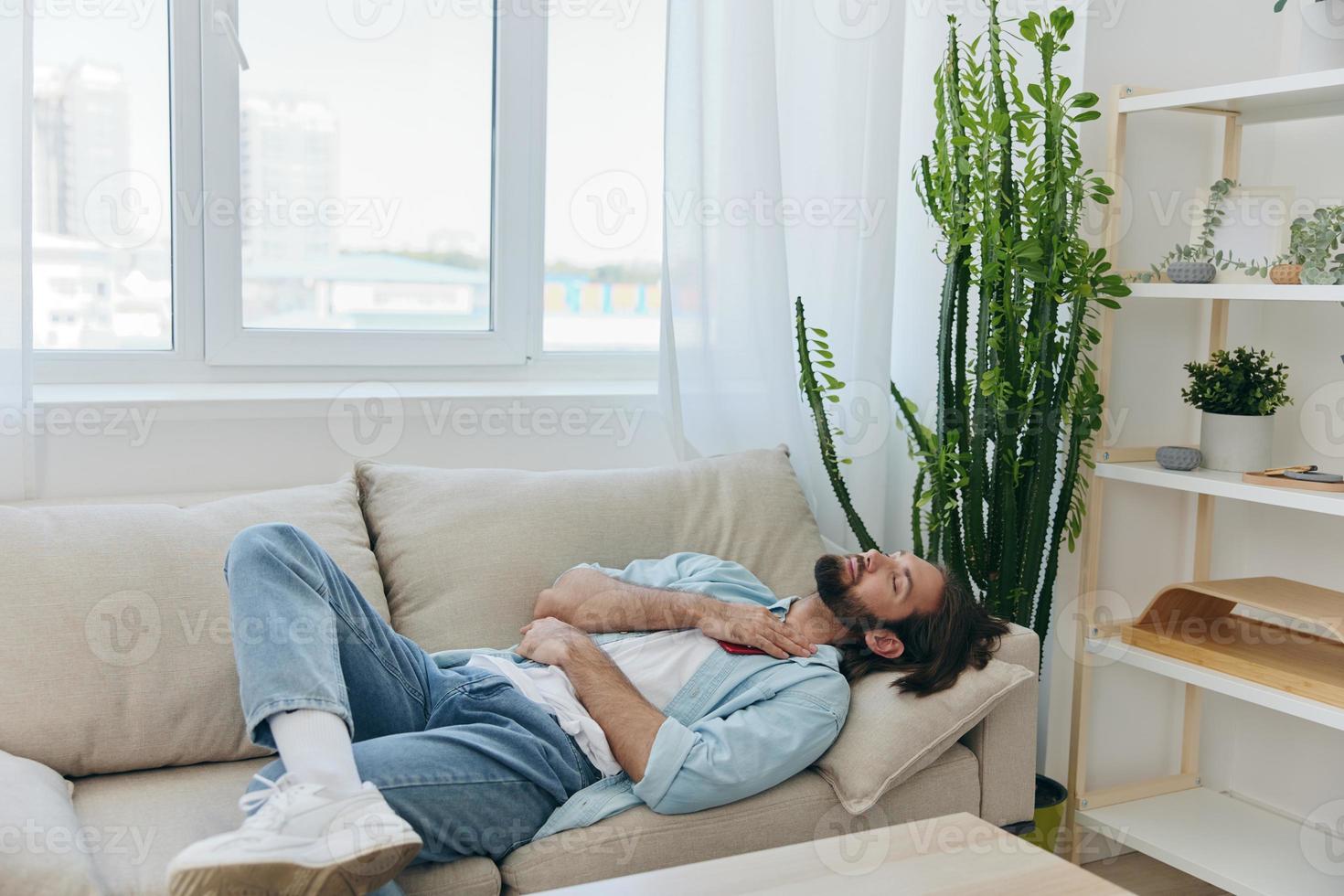 A man with a beard sleeps on the couch in the afternoon tired and relaxed after stress and ill health. Stress at work, poor sleep and health problems photo