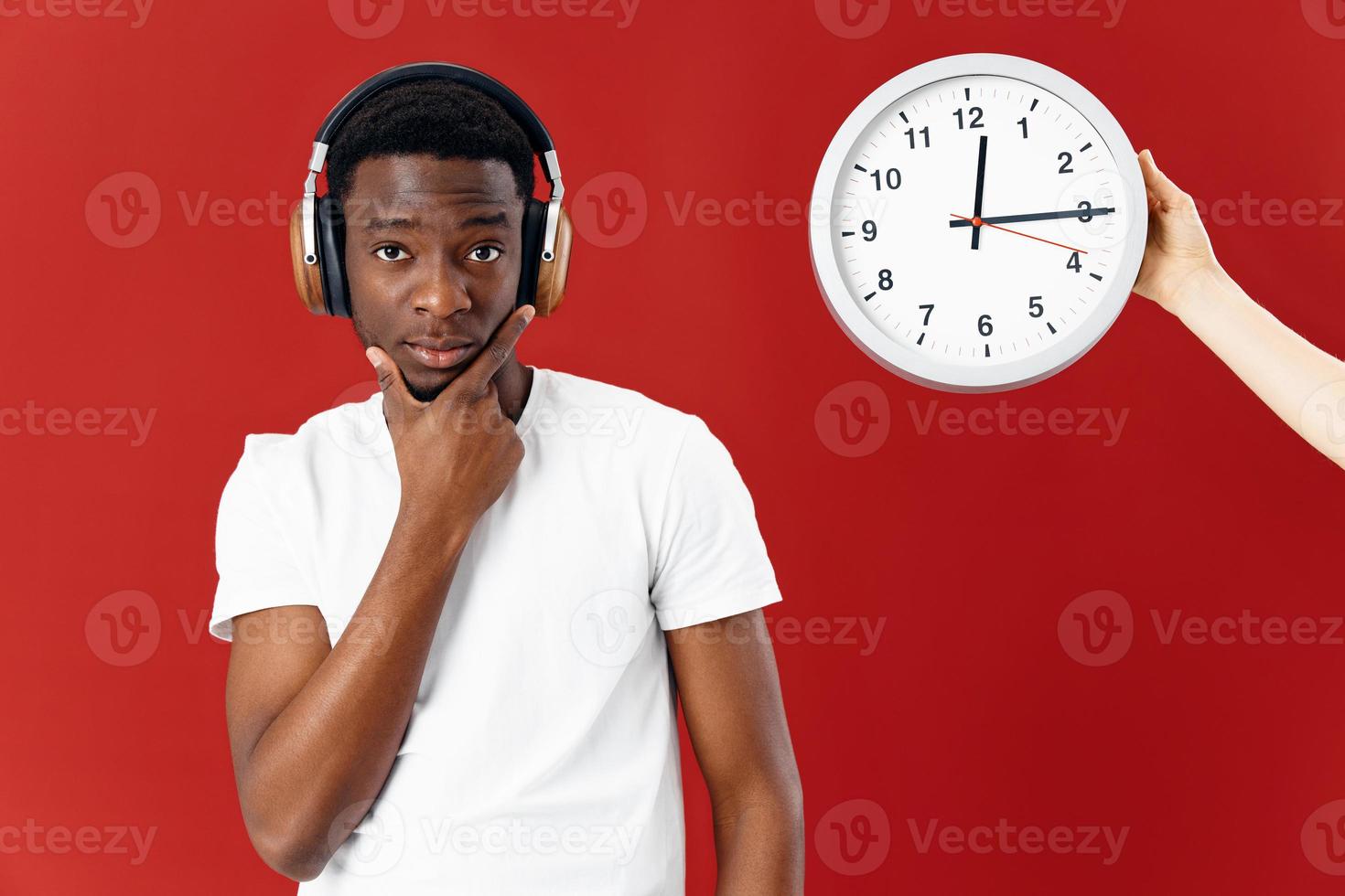 African American in headphones in a white t-shirt next to a clock red background photo