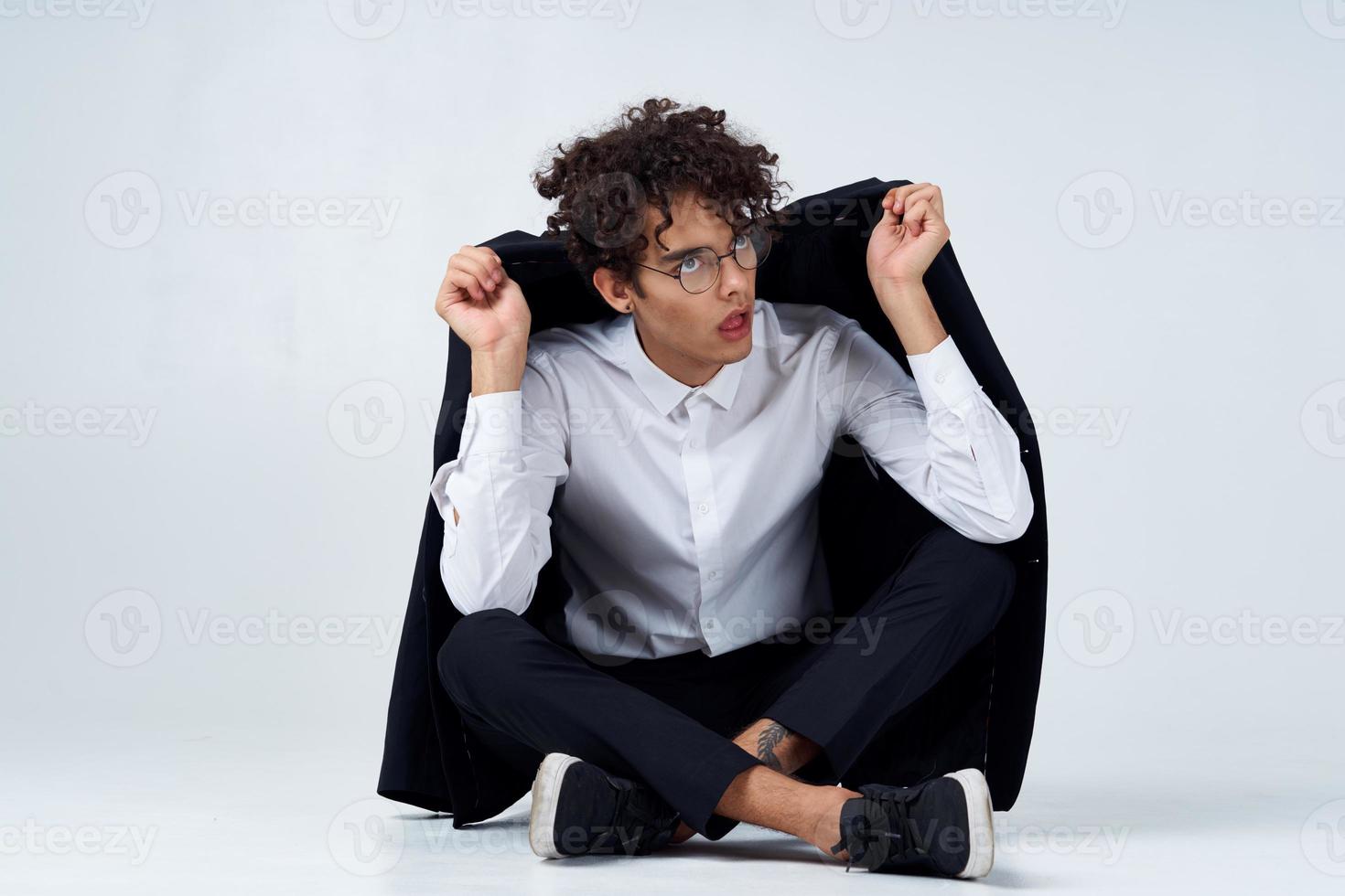 curly-haired guy straightens his jacket over his shoulders and sits on the floor in sneakers and in a suit photo