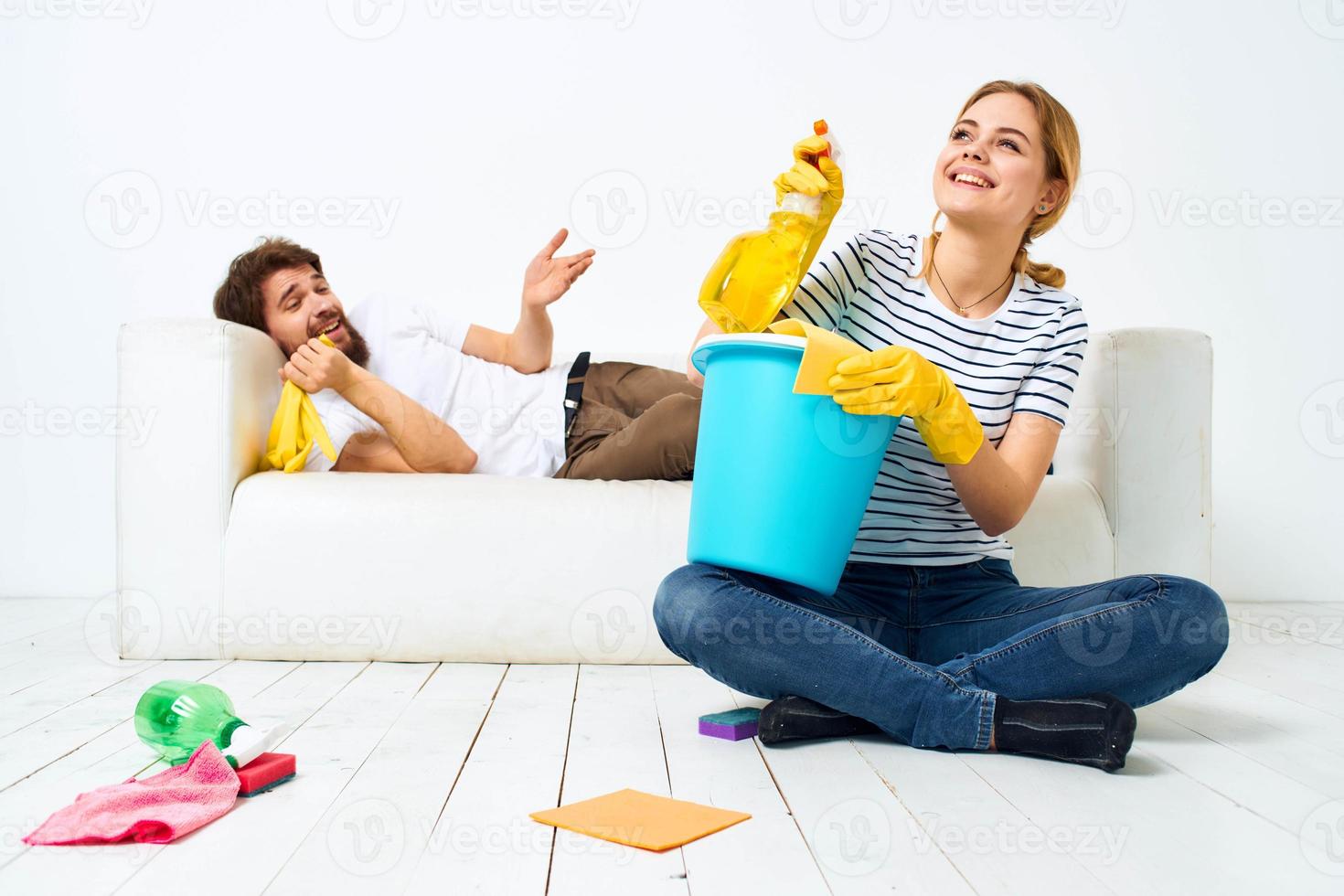 woman with a bucket in rubber gloves at home husband lies on the couch cleaning photo