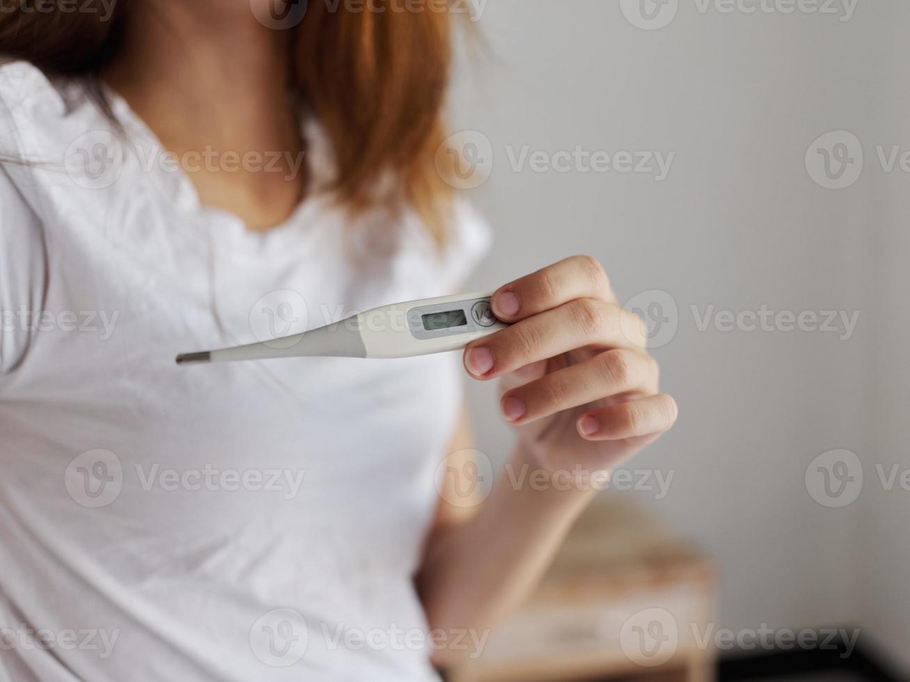 termómetro en el manos de un mujer en un blanco camiseta temperatura cheque foto