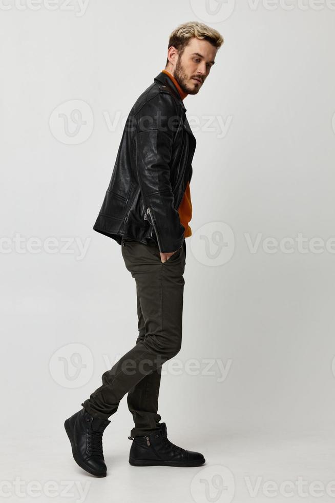 a man in a leather jacket, orange sweater and trousers turned to the side on a Light background copy Copy Space photo
