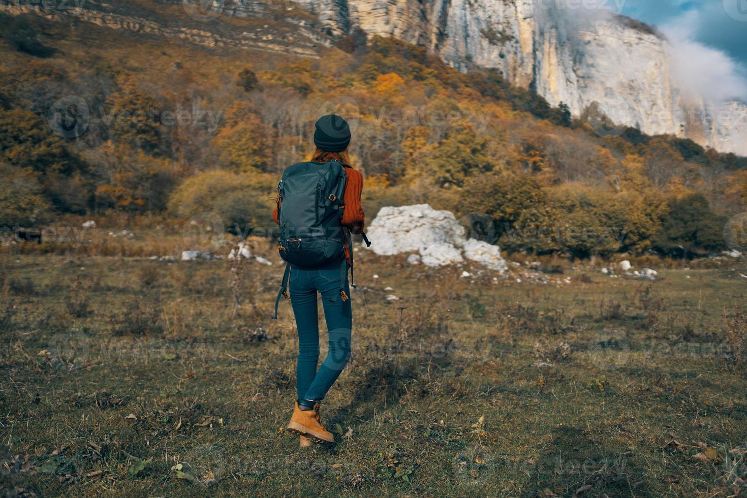 woman in jeans boots and a sweater with a backpack are resting in the autumn in the mountains in nature photo
