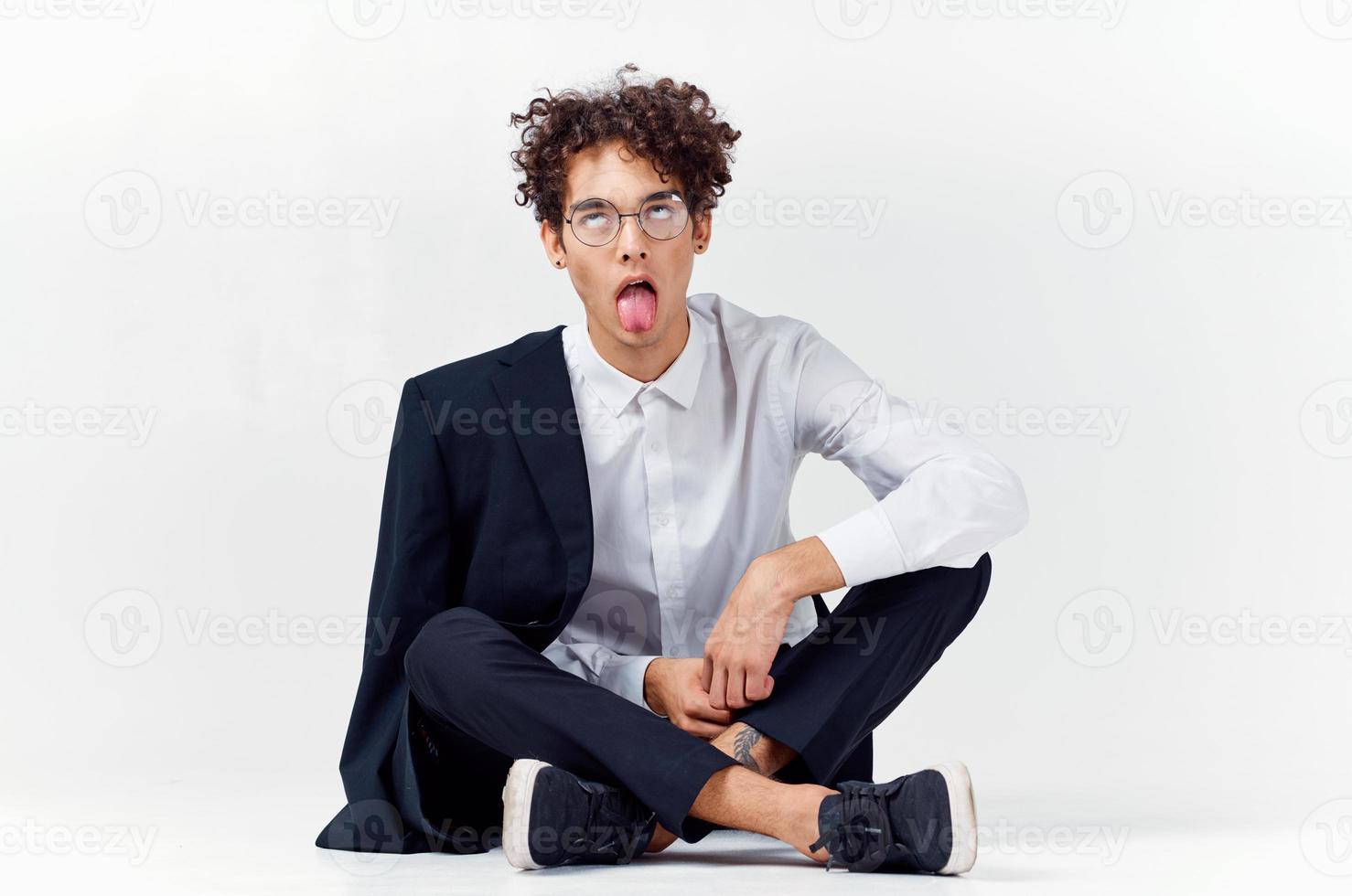 elegante joven hombre con Rizado pelo y en un clásico traje en un ligero antecedentes foto