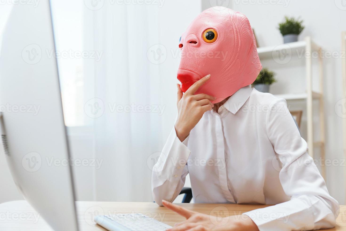 Thoughtful crazy businesswoman worker freelancer in pink fish mask work on computer online pondering or making decision thinking of problem solution touch head in light modern office. Copy space photo