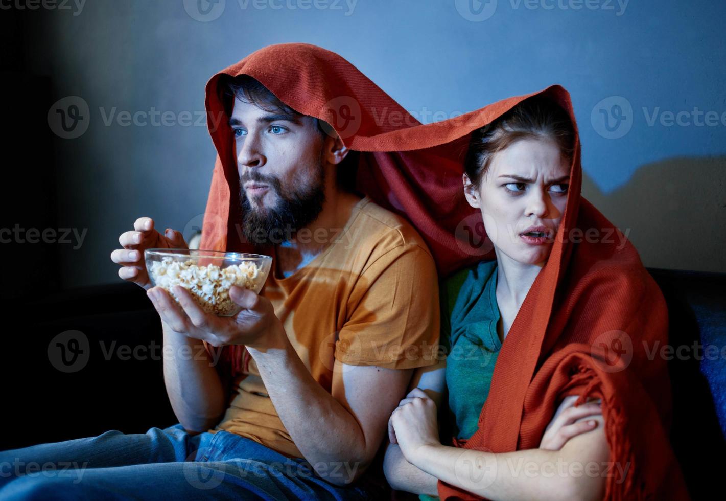 scared woman with a red plaid on her head and a man with a plate of popcorn in a dark room photo