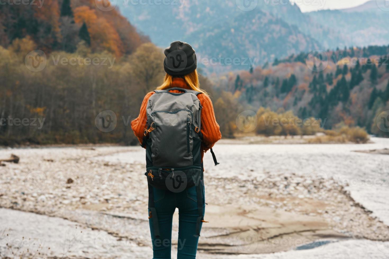 woman travels in the mountains in autumn near the river in nature with a backpack back view photo