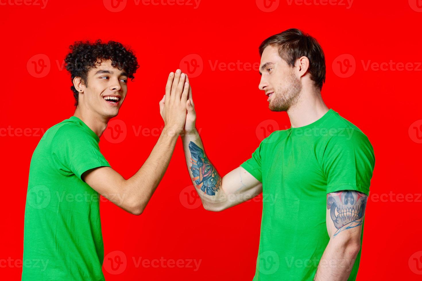 two friends in green t-shirts communication red background studio photo