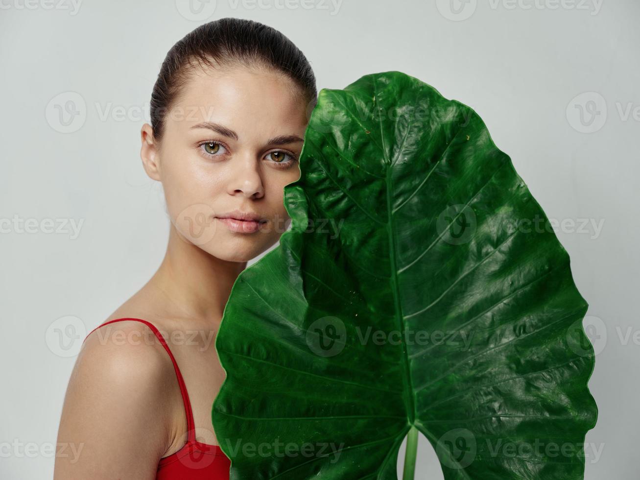 un mujer en un rojo camiseta en un ligero antecedentes sostiene un verde hoja en su manos campo natural Mira foto