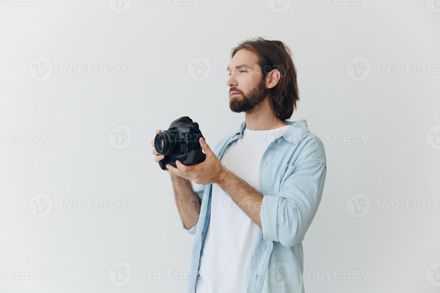 A male hipster photographer in a studio against a white background looks through the camera viewfinder and shoots shots with natural light from the window. Lifestyle work as a freelance photographer photo