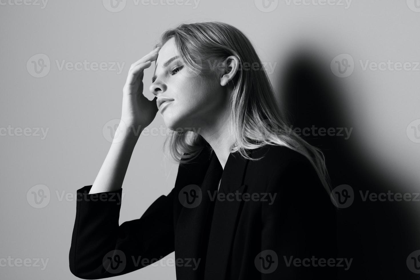 Aesthetic pensive sad blonde young model posing in classic jacket touching stocking hair at studio. Beautiful lady thoughtful looking and caress her curls. Black and White concept photo