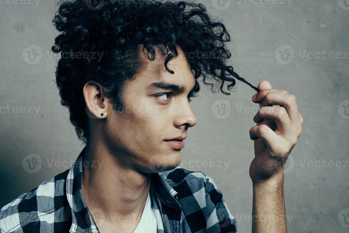 guy in a t-shirt and in a plaid shirt examines his hair on a gray background cropped view close-up photo