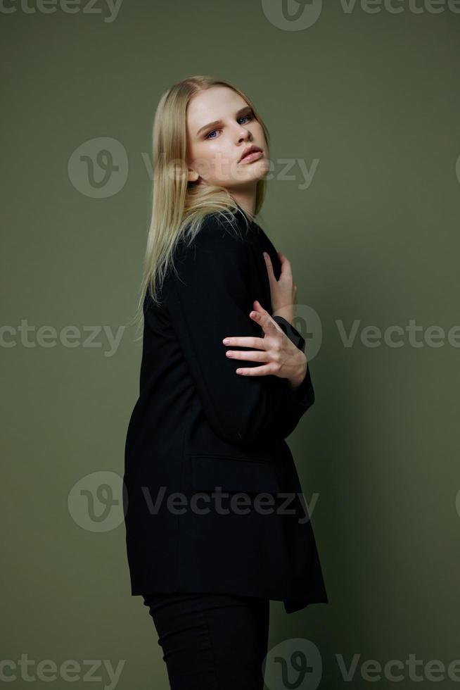Art fashion photo shoot. Professional blonde model holds herself hugs with both hands half-turned looks at the camera posing on a green background in the studio