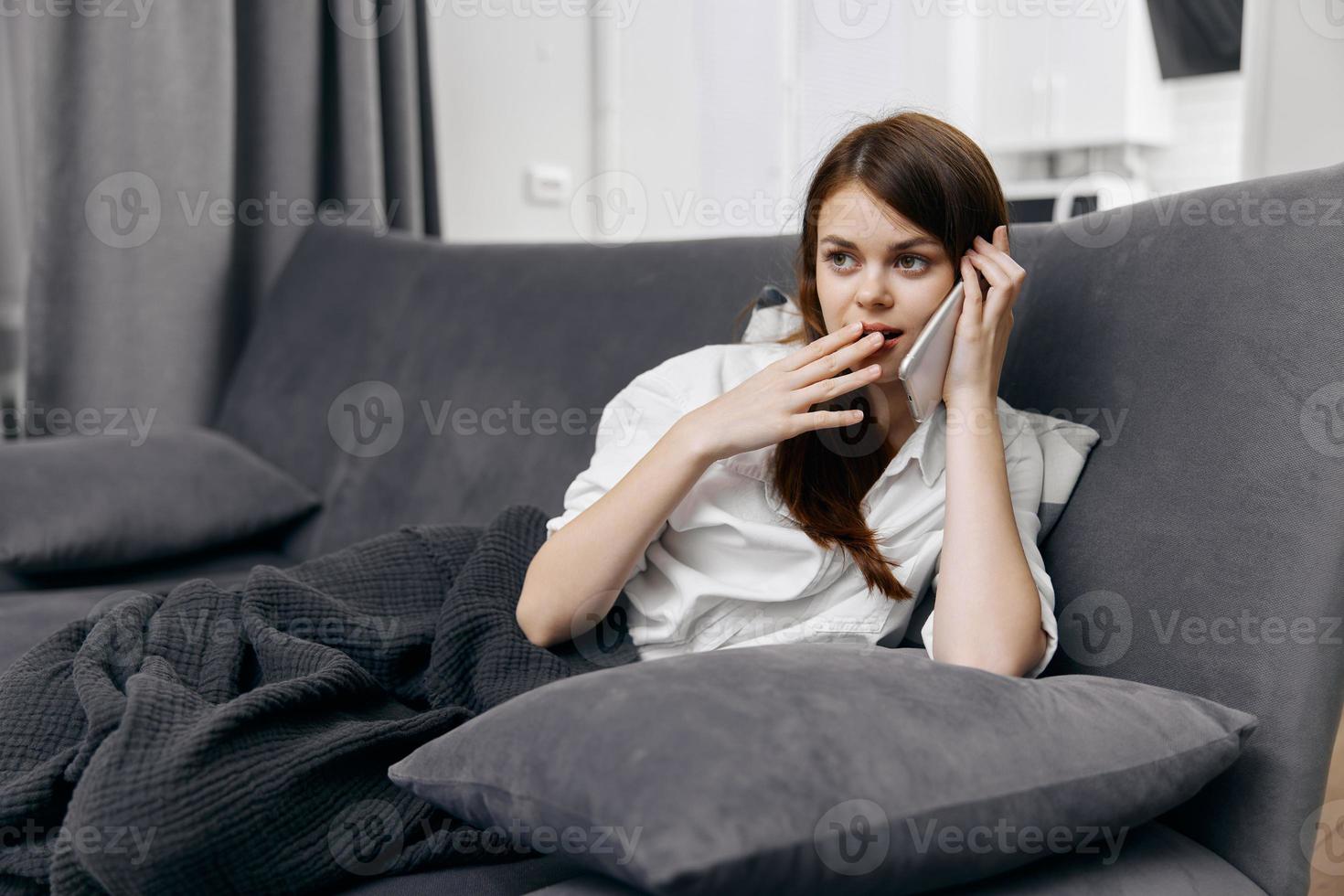 woman talking on the phone and sitting on the couch with a blanket on her lap photo