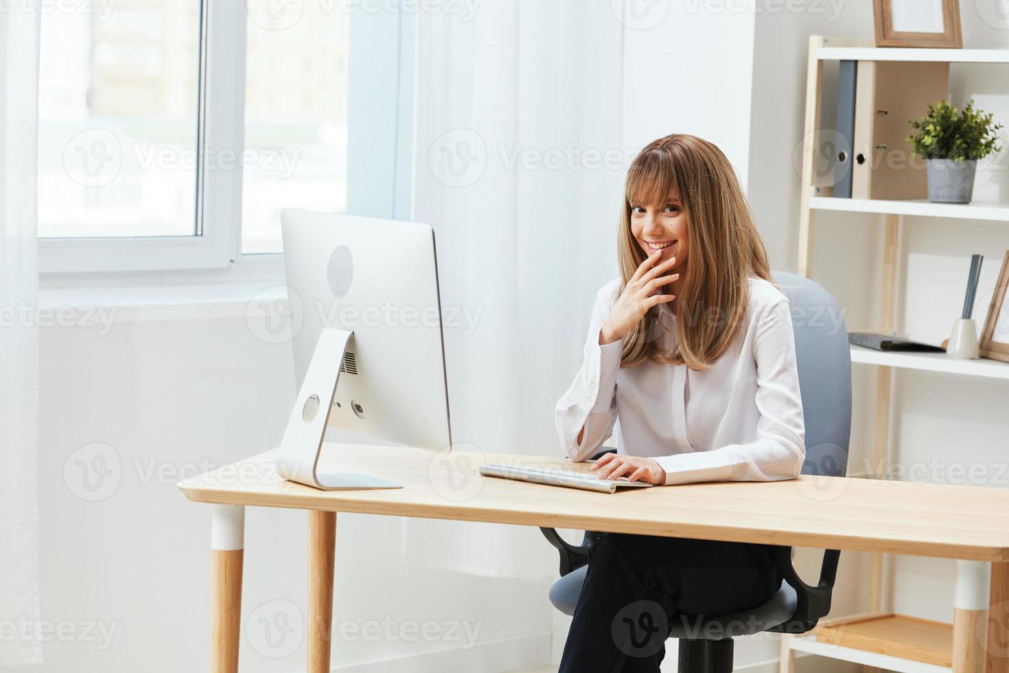 Happy smiling adorable blonde businesswoman worker freelancer look at camera sitting at workplace in light modern office. Cheerful employee work on computer online in support service. Copy space photo