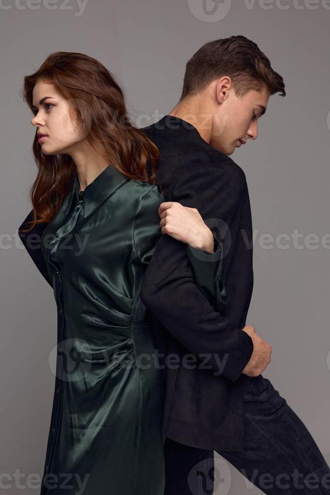 An elegant woman holds the hand of a man in a suit on a gray background with backs to each other photo