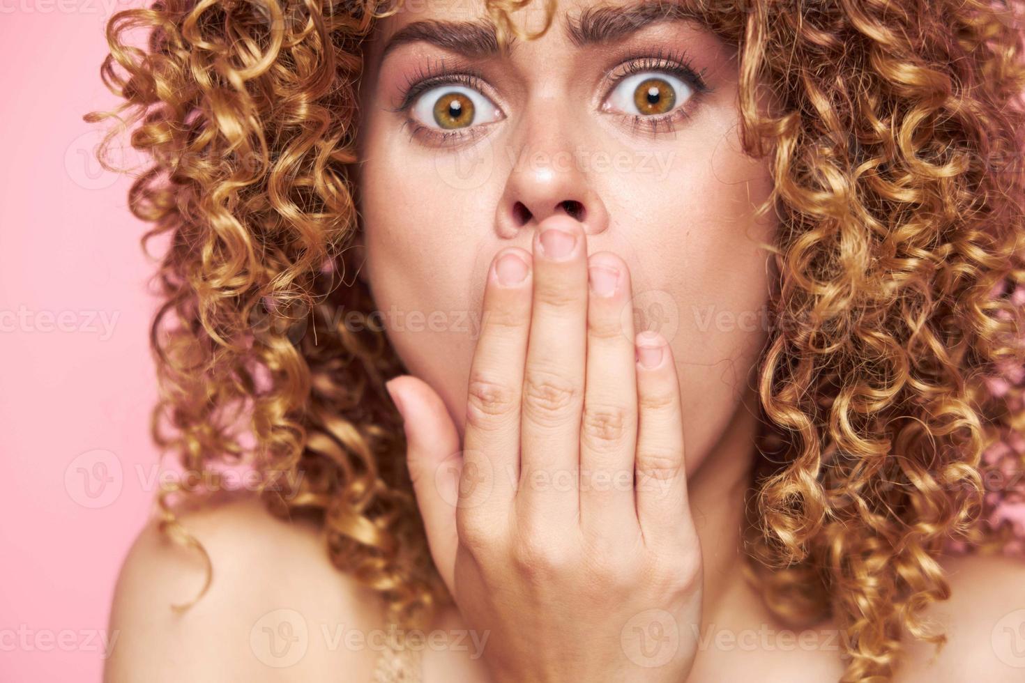 Beautiful woman looking at the camera in surprise and covering her mouth with her hands bright makeup pink background photo