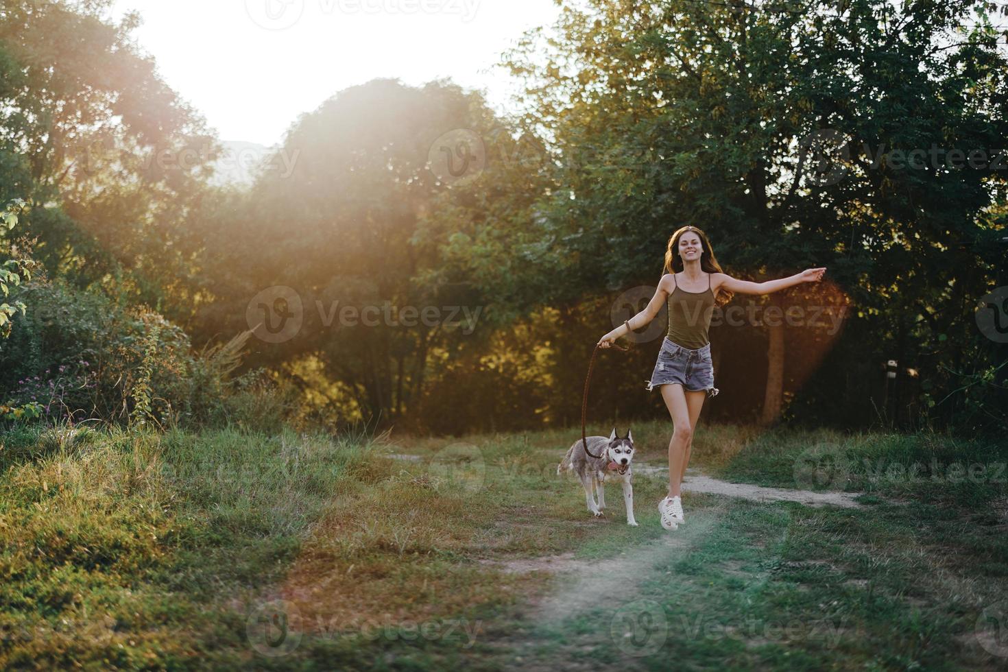 A woman runs with a dog in the forest during an evening walk in the forest at sunset in autumn. Lifestyle sports training with your beloved dog photo