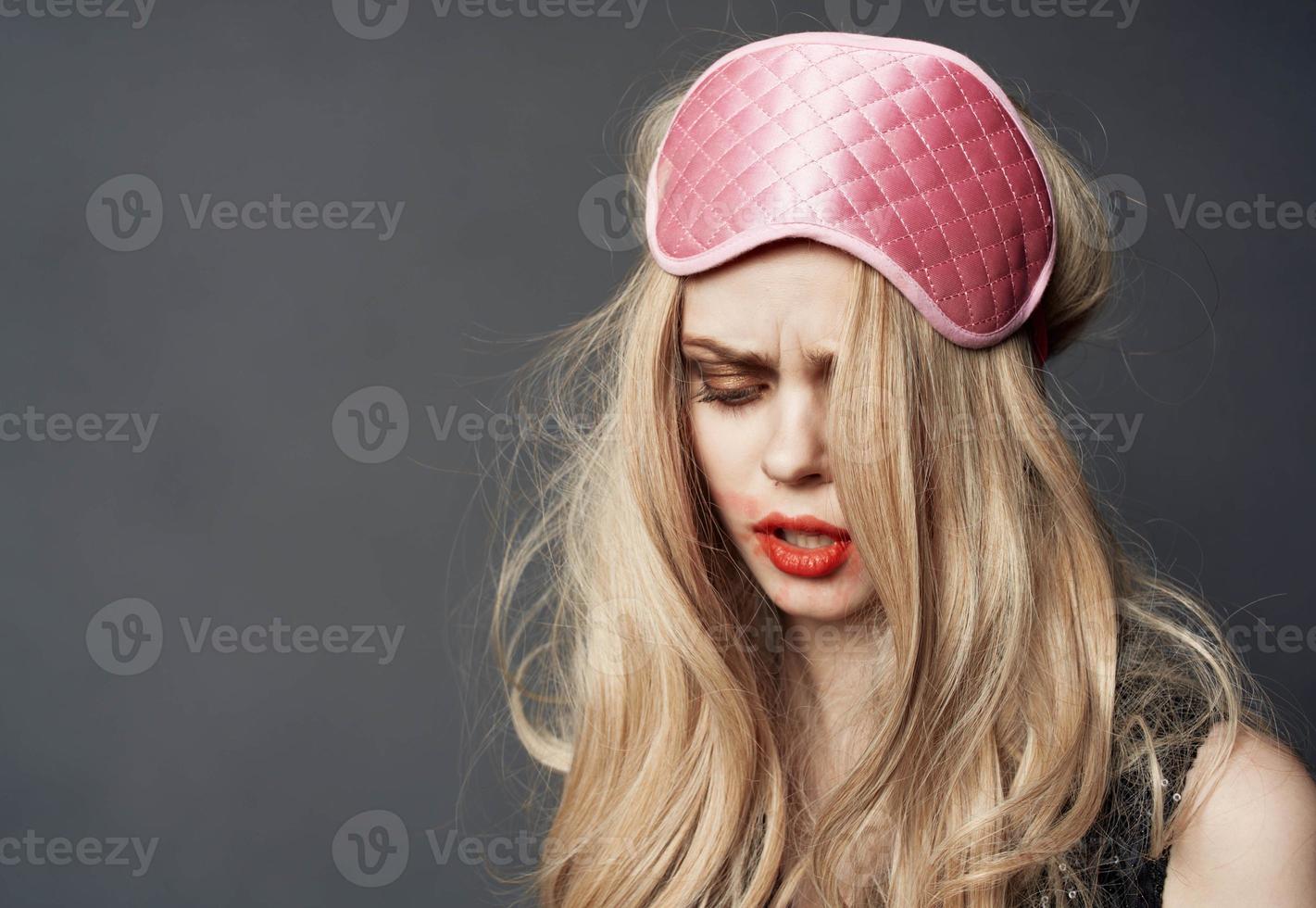 portrait of a blonde in a sleep mask and bright makeup lipstick smeared on her face photo