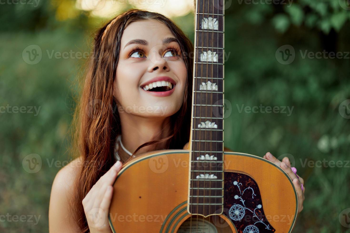 joven hippie mujer con eco imagen sonriente y mirando dentro el cámara con guitarra en mano en naturaleza en un viaje foto