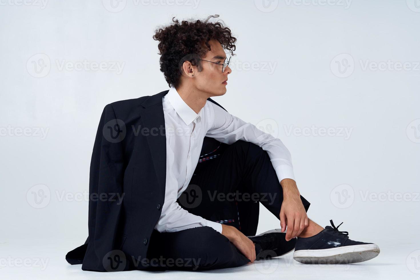 stylish man with curly hair in sneakers on a light background a jacket on the shoulder pants model photo