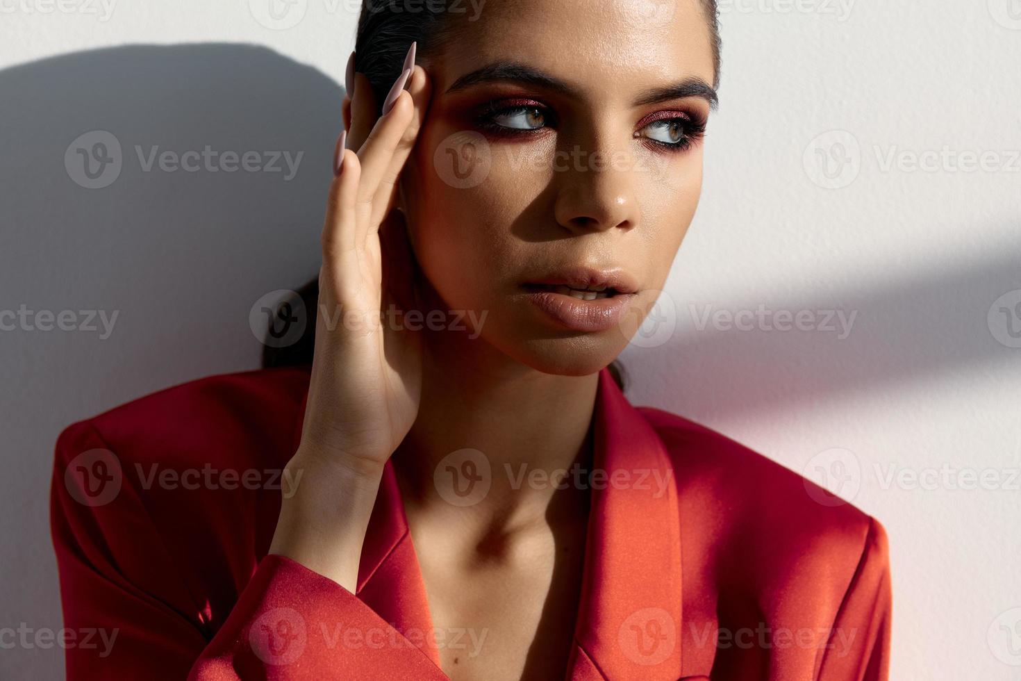 mujer en un rojo chaqueta sostiene un mano cerca el cara en un ligero antecedentes Moda estilo foto
