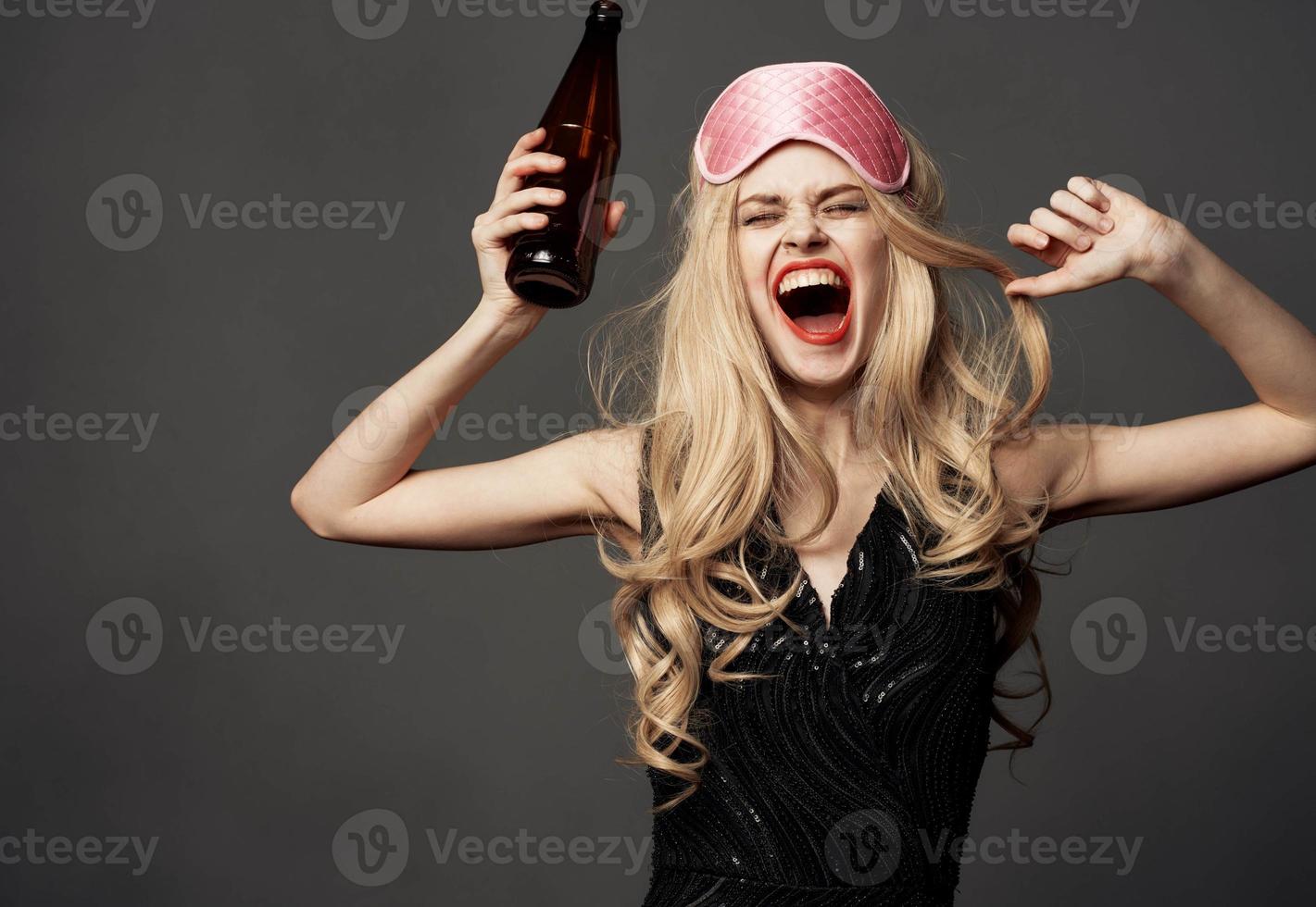 Women with a pink sleep mask holds a bottle of beer in her hand photo