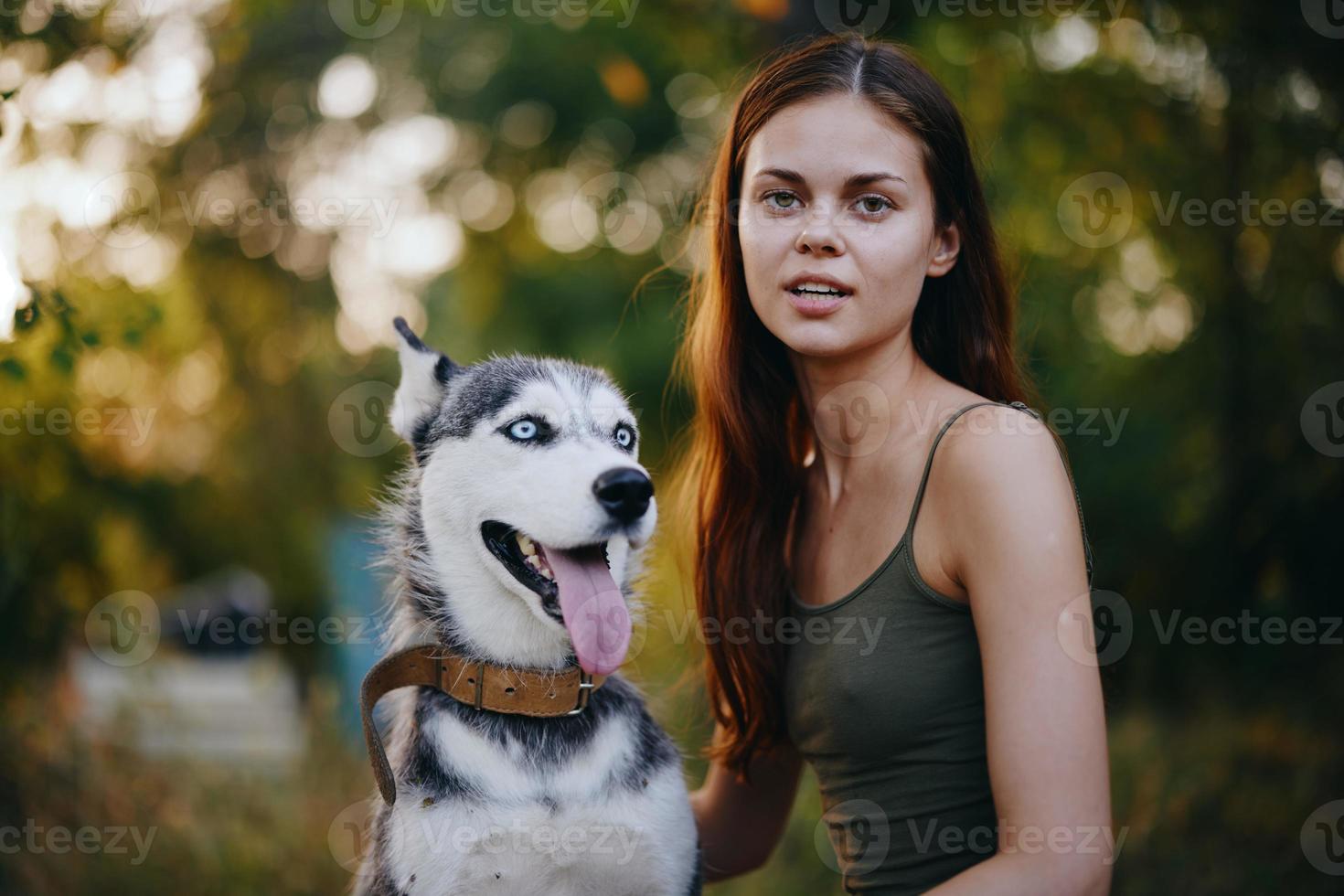 A woman with a husky breed dog smiles and affectionately strokes her beloved dog while walking in nature in the park in autumn against the backdrop of sunset photo