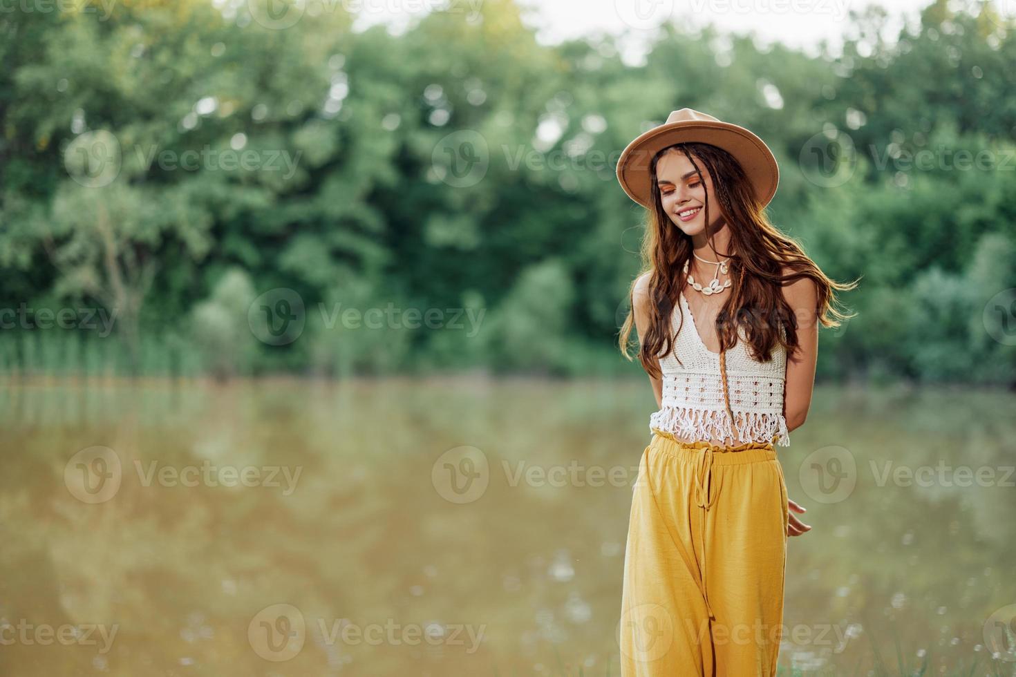 A young woman in a hippie look travels in nature by the lake wearing a hat and yellow pants in the fall photo