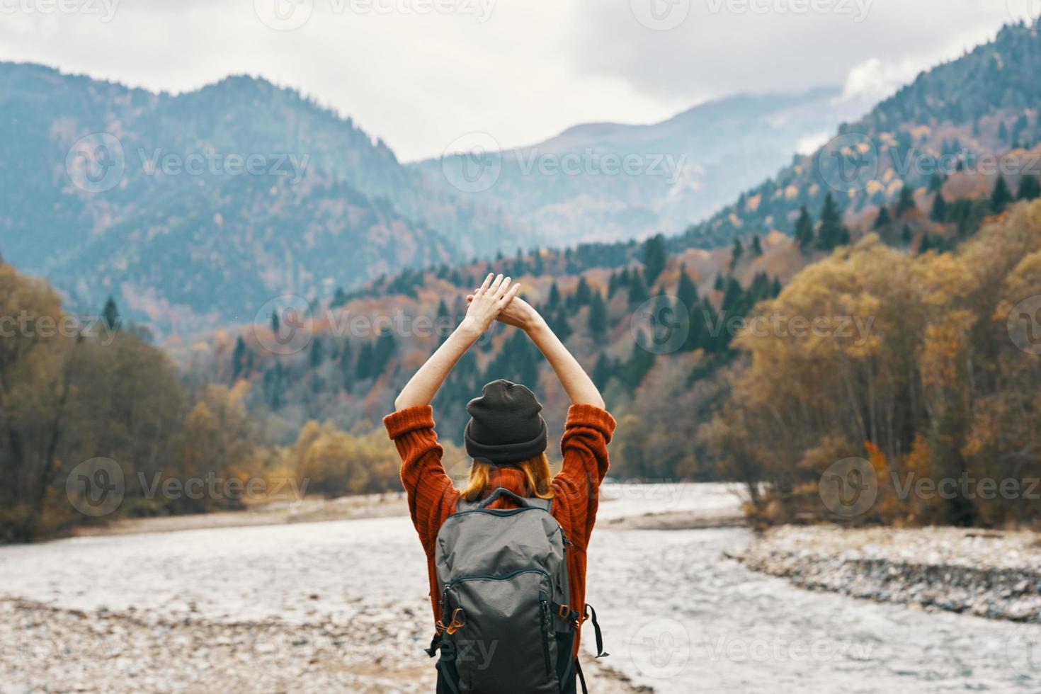 happy woman in the mountains travels near the river in nature and raised her hands up photo