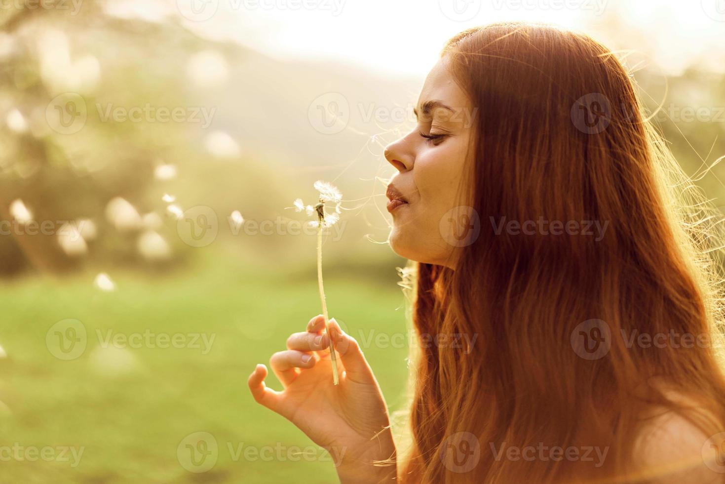 un joven mujer sostiene un diente de león en su manos y golpes en él, el semillas de el diente de león mosca mediante el aire a crecer nuevo flores cuidando para el la tierra ecología foto