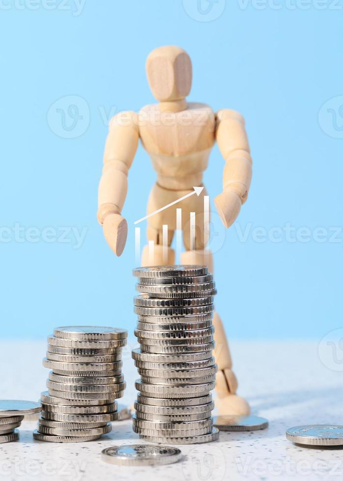 Wooden mannequin and a stack of coins on a blue background. Business indicators growth concept, income growth photo