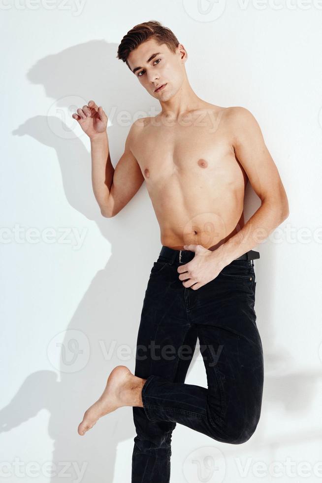 The guy is standing on one leg in black trousers and a naked torso photo