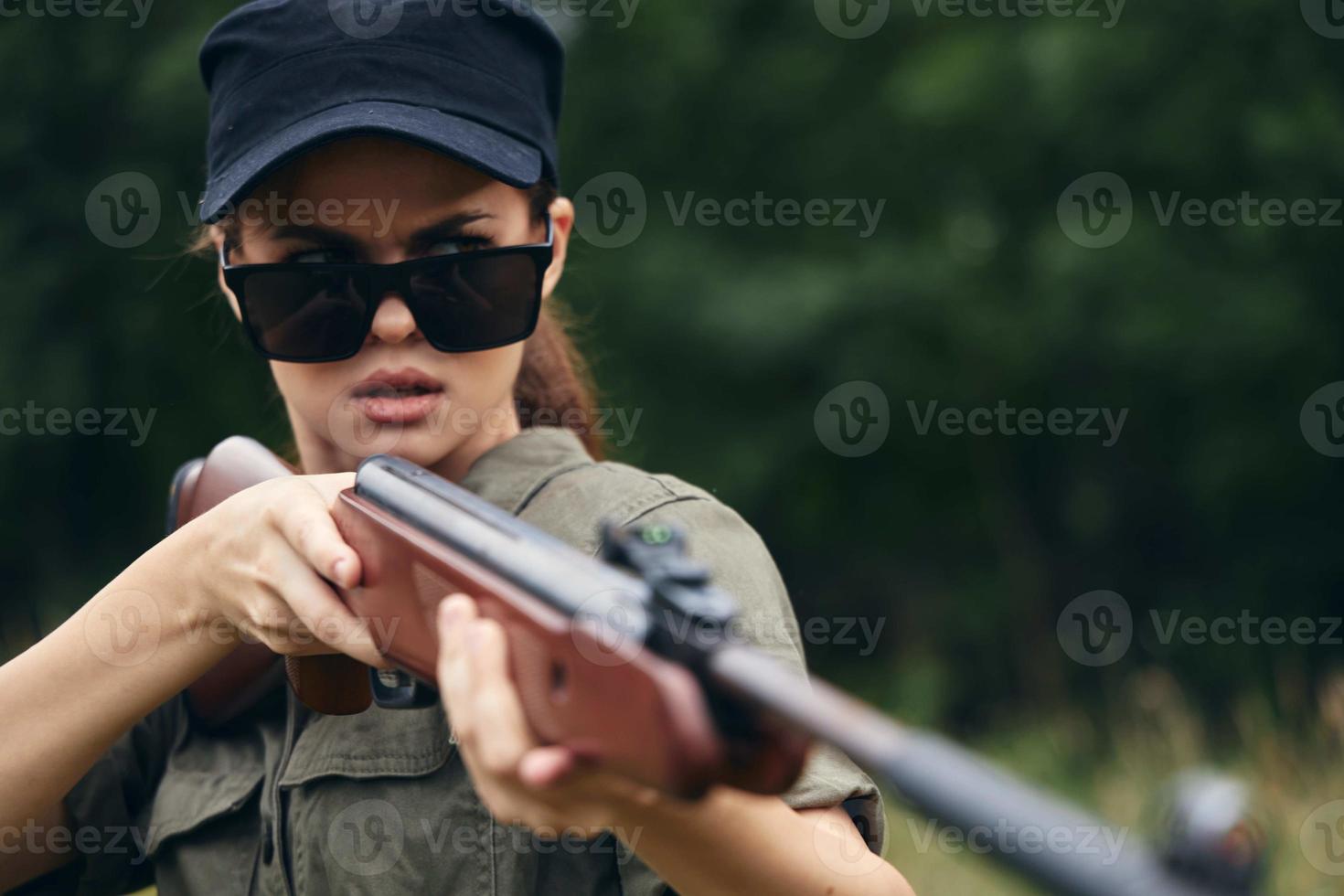 mujer soldado con armas en mano, Gafas de sol, puntería caza verde hojas foto