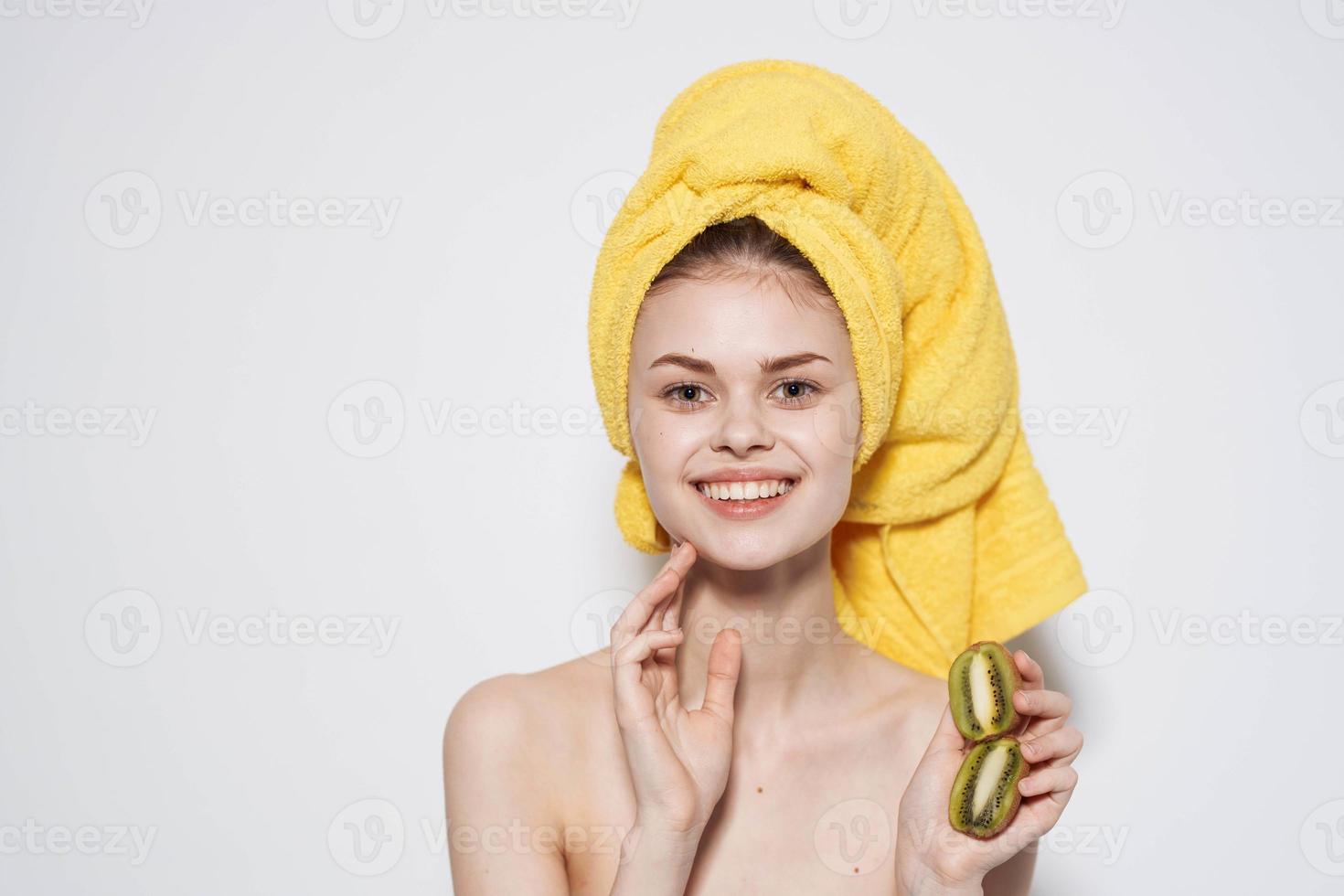 Cheerful woman with bare shoulders QIWI in hands with a towel on her head cropped view light background photo