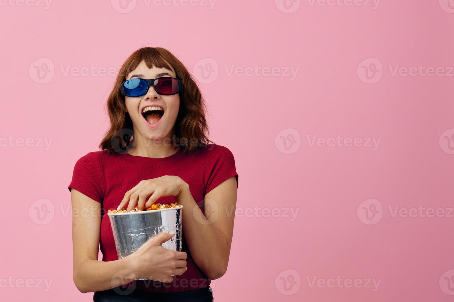 Overjoyed happy cute redhead lady in red t-shirt 3D glasses with popcorn watch movie posing isolated on over pink studio background. Copy space Banner. Fashion Cinema concept. Entertainment offer photo