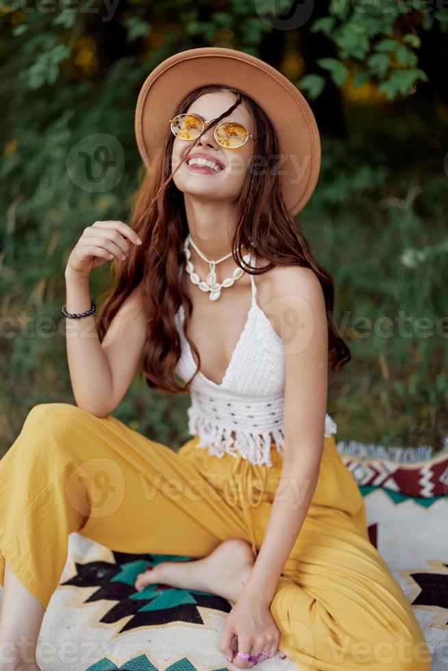 Hippie woman in eco clothing laughs and wiggles as she sits on a plaid outside in the fall with a hat and yellow sunglasses photo