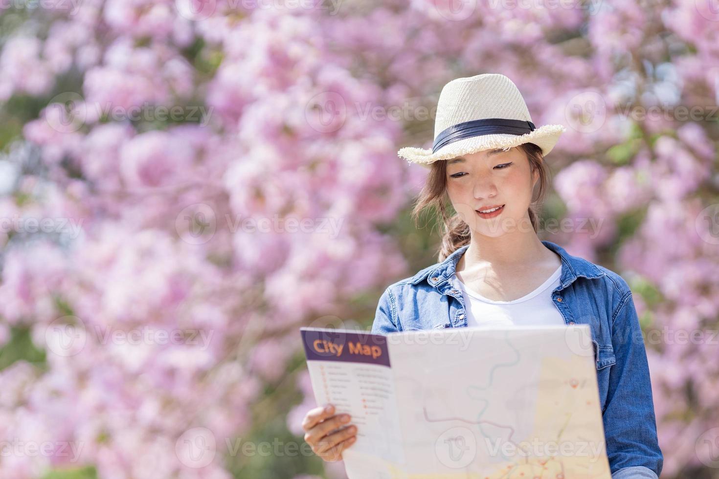 Asian woman tourist holding city map while walking in the park at cherry blossom tree during spring sakura flower festival concept photo