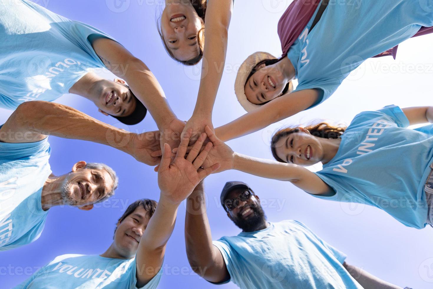 Team of young and diversity volunteer worker group enjoy charitable social work outdoor together in saving environment project wearing blue t-shirt while joining hand in power assemble unity concept photo