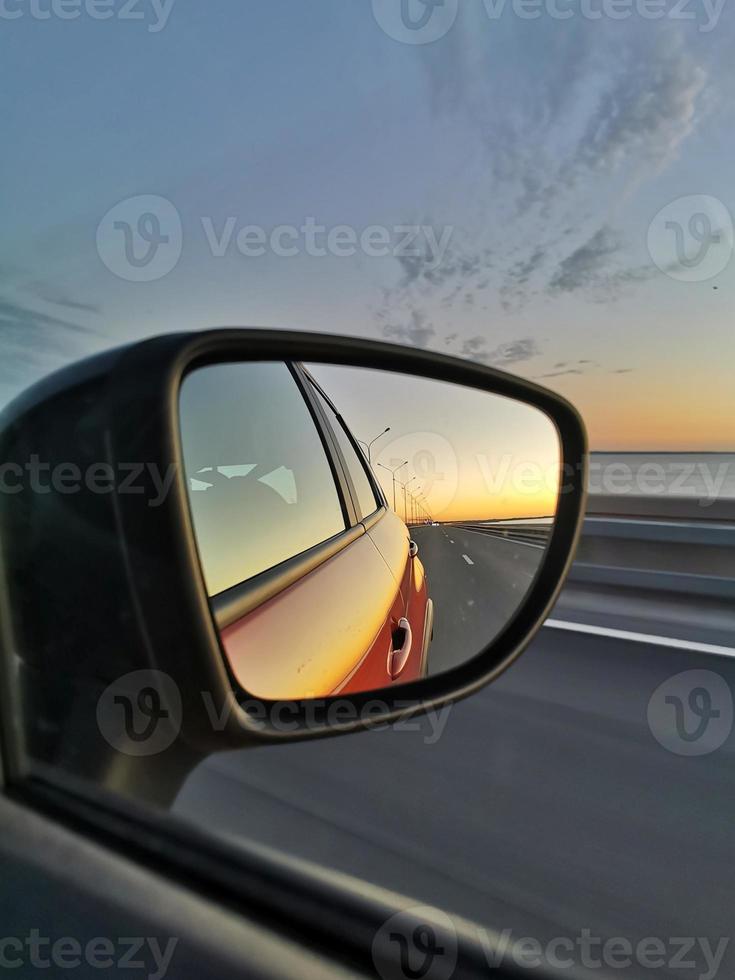 Reflection of road and sunset in the side mirror of the orange car. Concept of road trip and traveling by car. photo