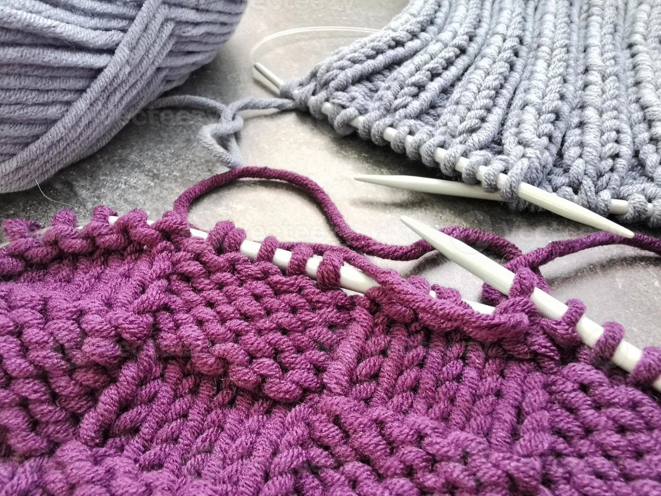 Gray and purple pieces of knitting and skeins of yarn on gray background. Knitted patterns and textures close up. Handmade and needlework hobbies. photo