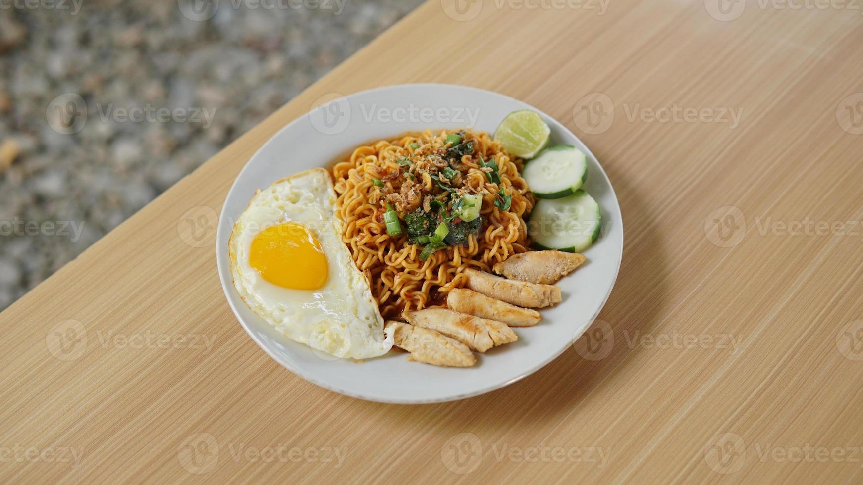 Fried instant noodle with chicken cutlet and fried egg on wooden table