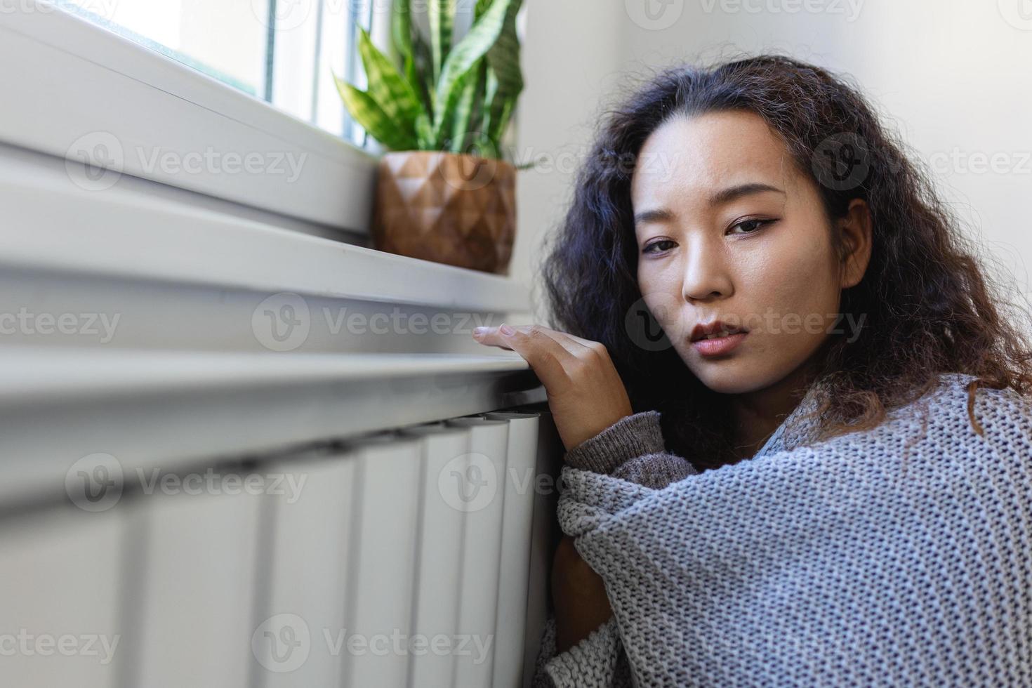 Unwell Asian woman renter in blanket sit in cold living room hand on