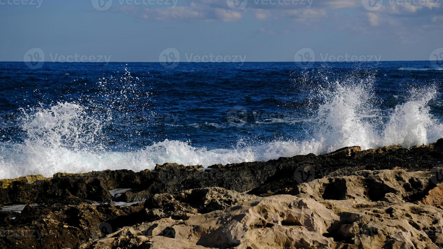 Blue sea wave and white foam and splash. Stone beach on island of Malta, no sandy beach. Summer holiday border frame concept. Tropical island vacation backdrop. Tourist travel banner design template. photo