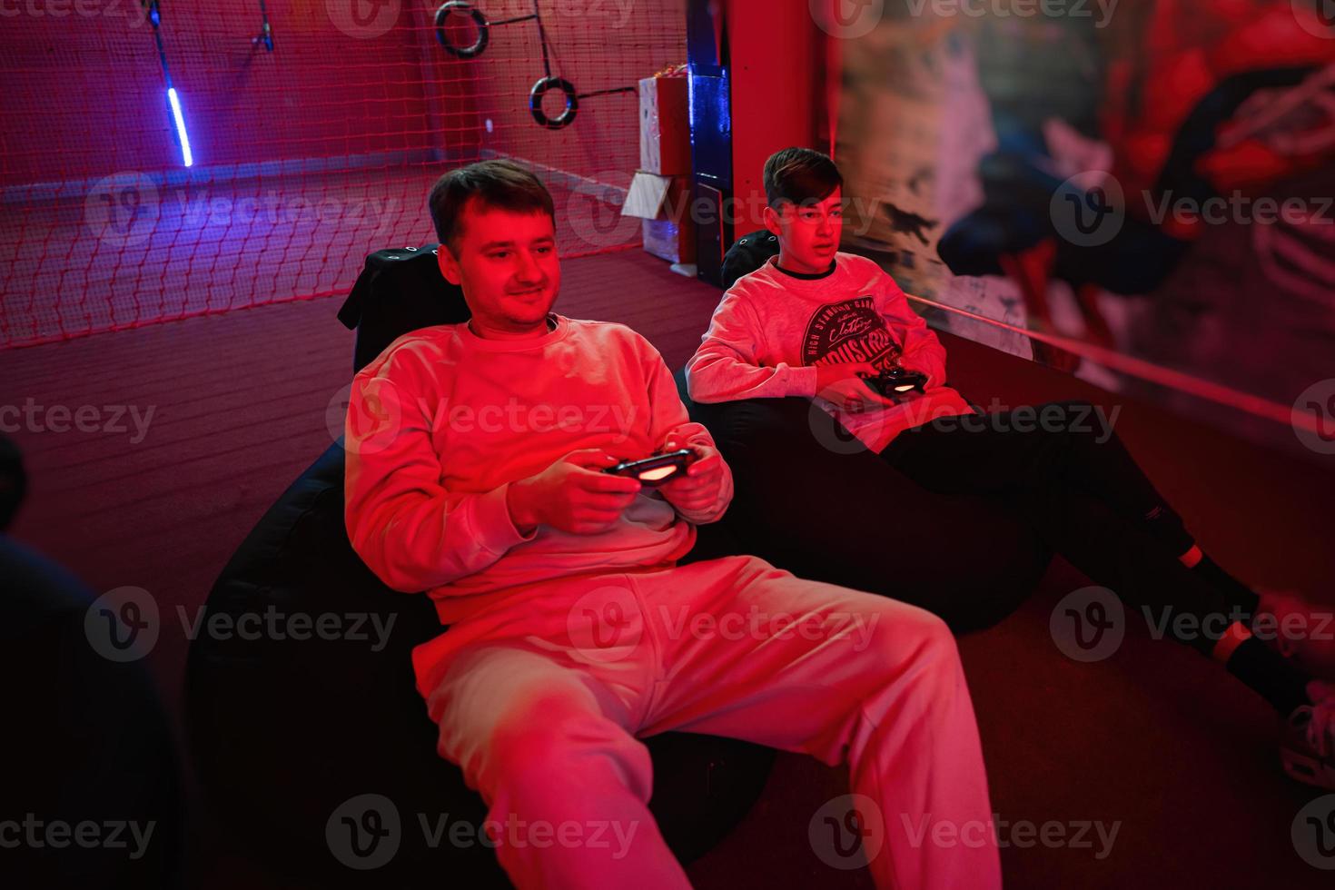 Father and son play gamepad video game console in red gaming room. Dad and kid gamers. photo