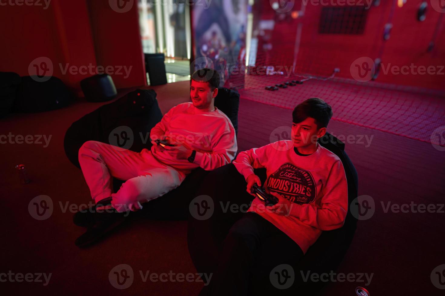 Father and son play gamepad video game console in red gaming room. Dad and kid gamers. photo