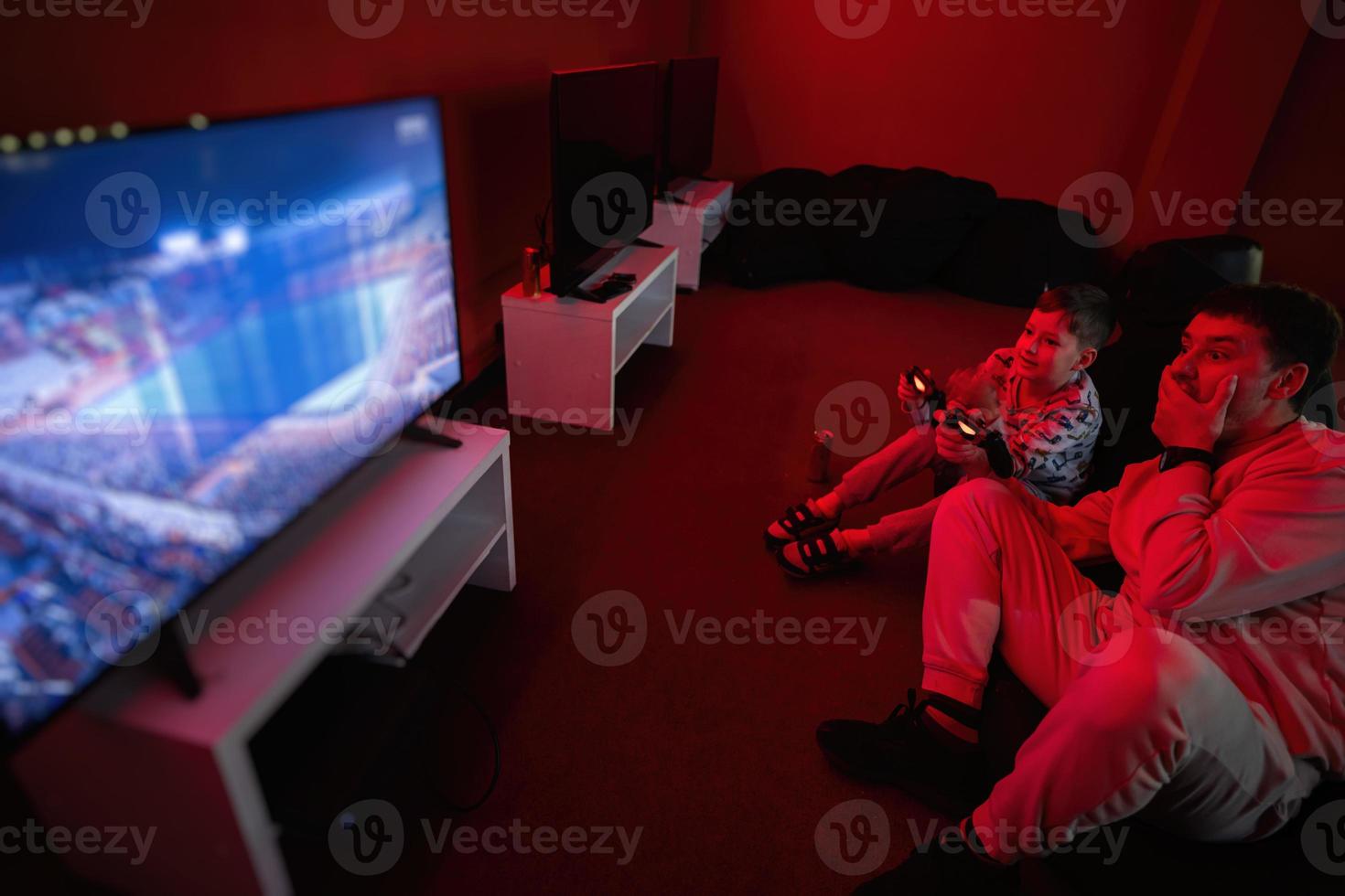 Father and son play gamepad video game console in red gaming room. Dad and kid gamers. photo