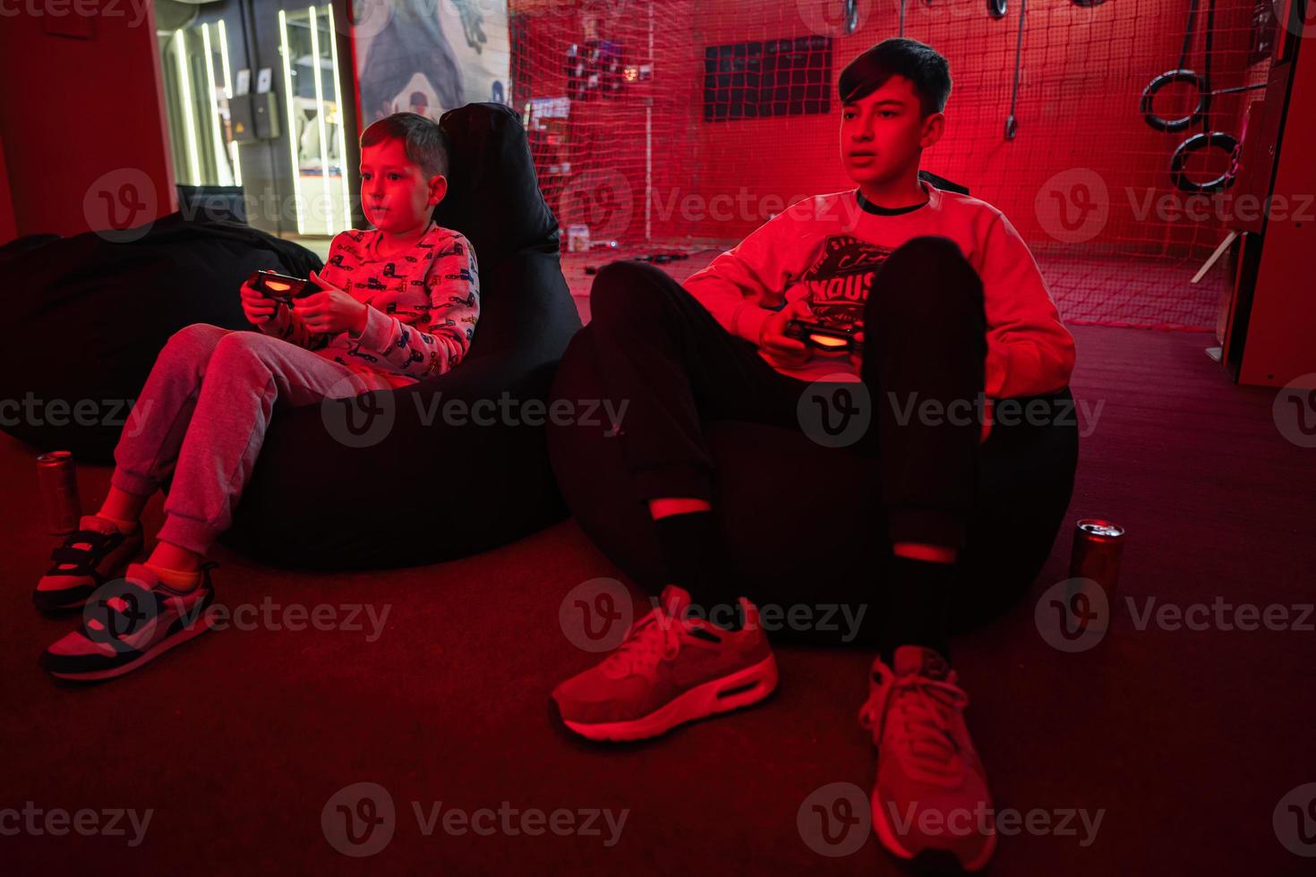 Two boys gamers play gamepad video game console in red gaming room. photo