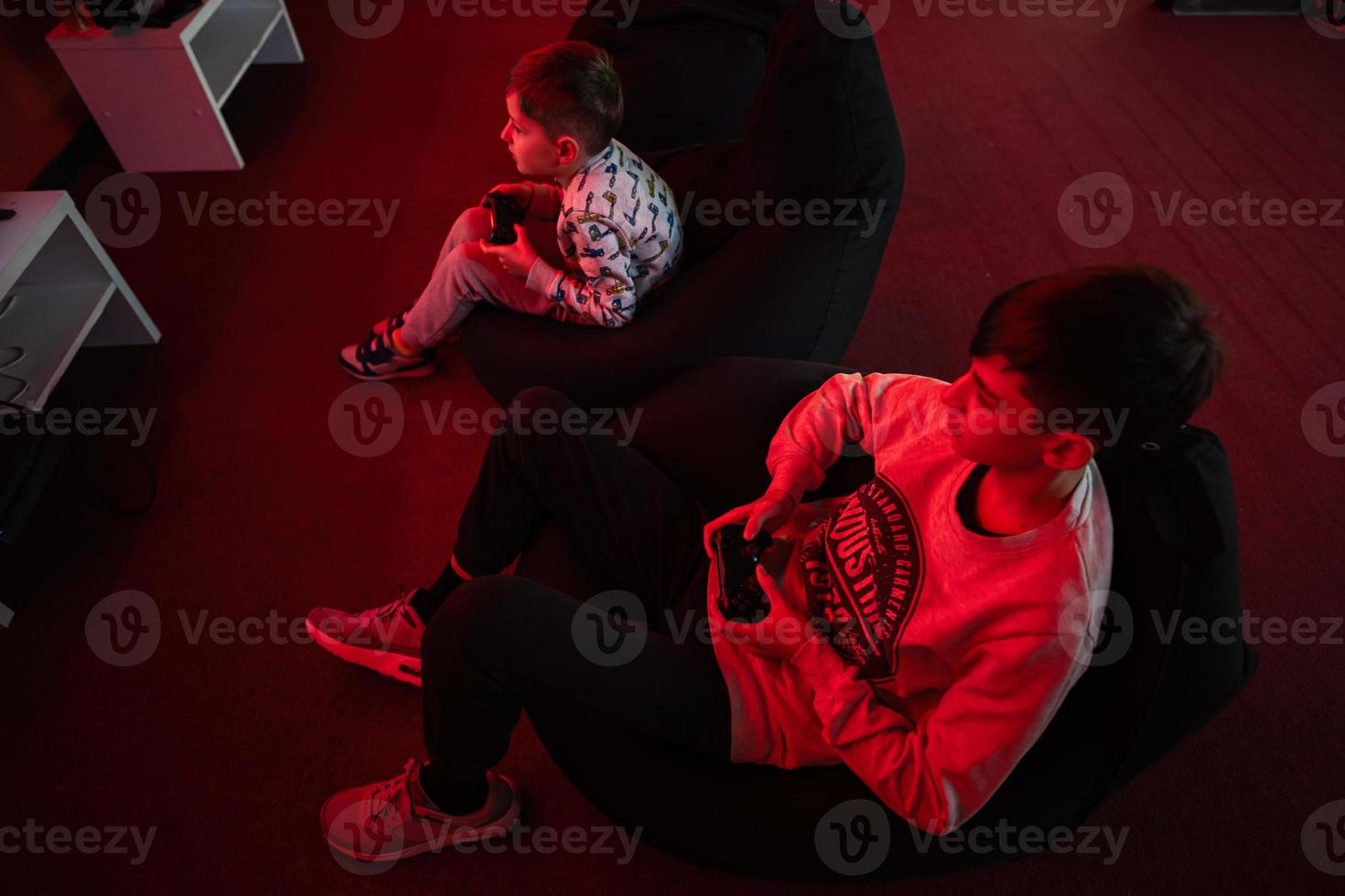 Two boys gamers play gamepad video game console in red gaming room. photo